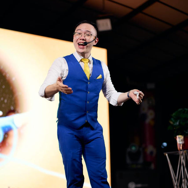 Man in a blue suit and yellow tie speaking on stage with a large screen behind him.